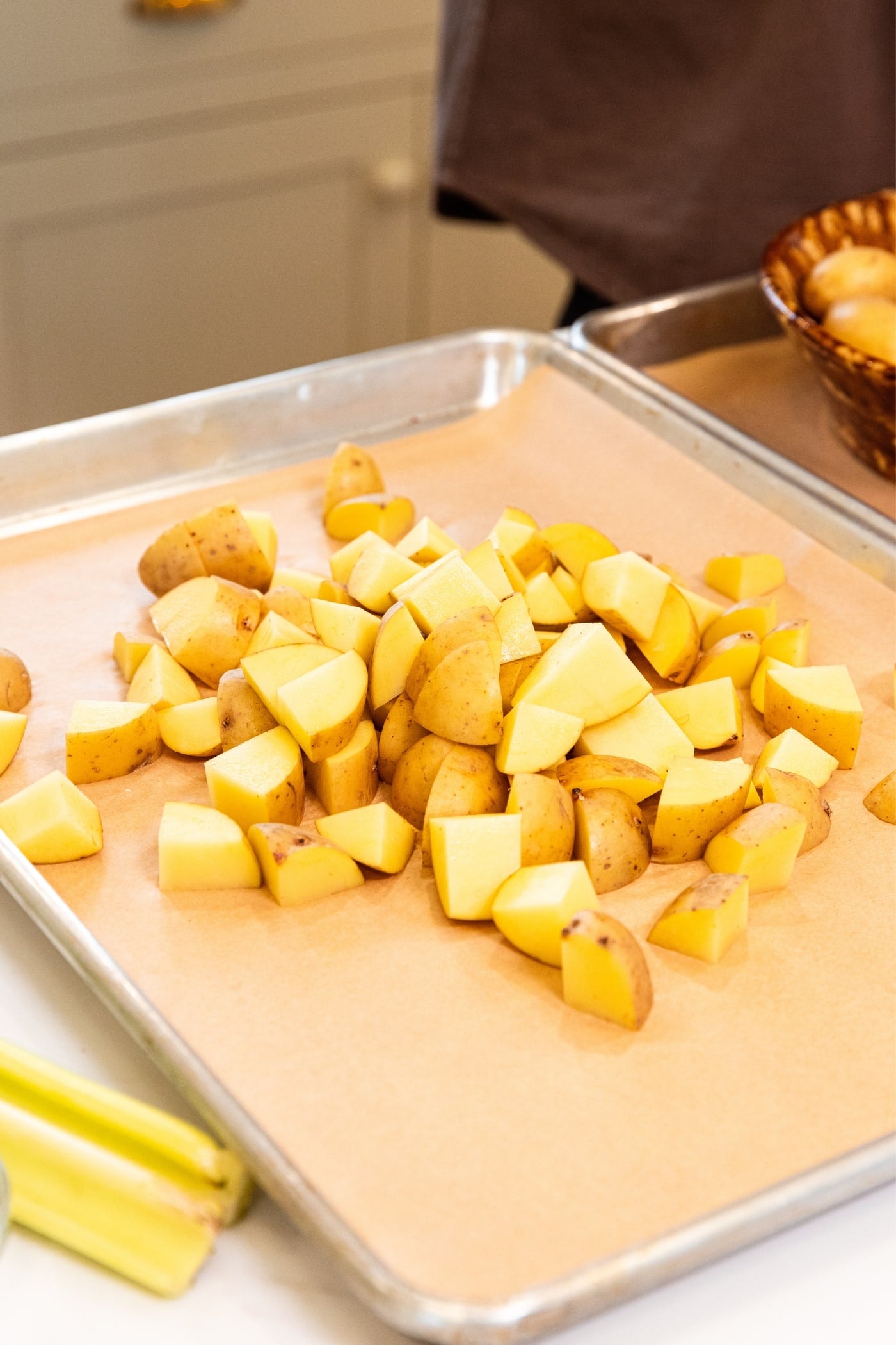 Parchment-lined baking sheet with pile of diced potatoes sitting on sheet before being shifted to an even layer.