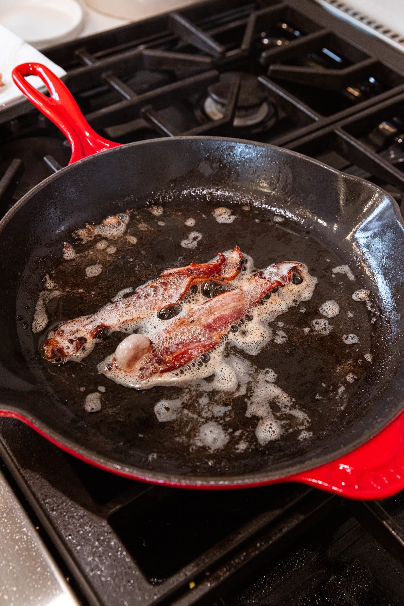 Red skillet filled with oil from fried bacon with two strips of bacon left in the pan.