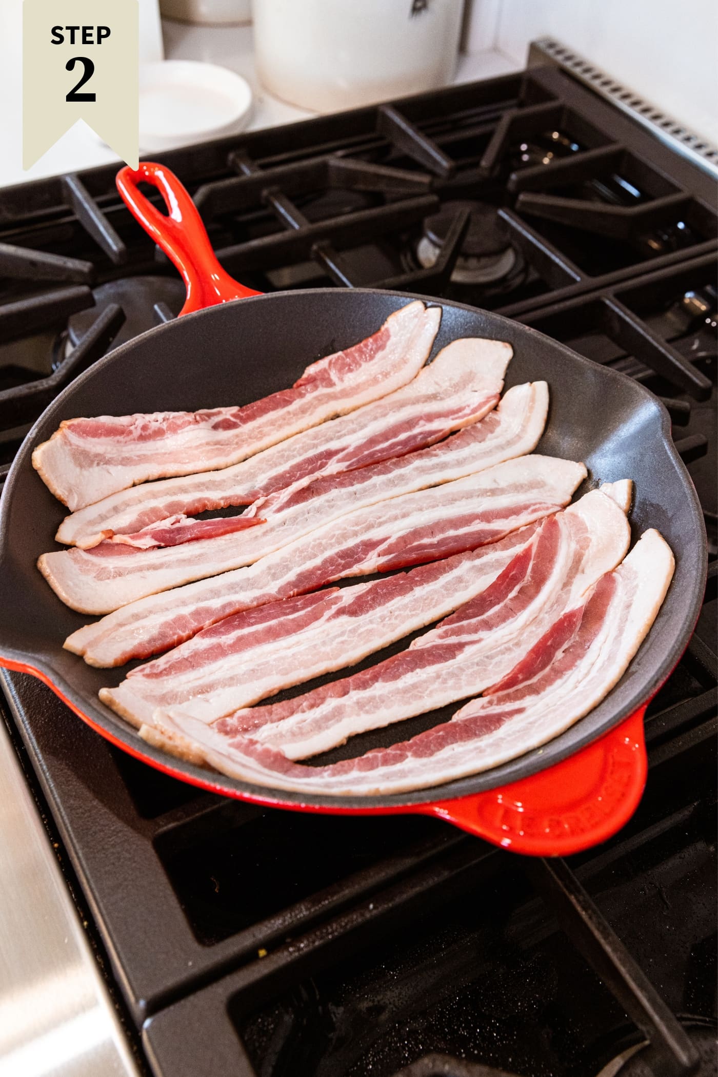 Pieces of uncooked raw bacon sitting in red skillet on stovetop right before beginning to cook.