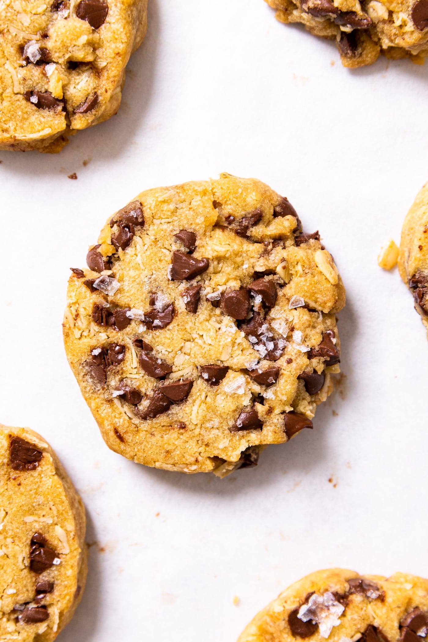 Top down view of baked chocolate chip refrigerator cookie sitting on white piece of parchment paper with sea salt on top