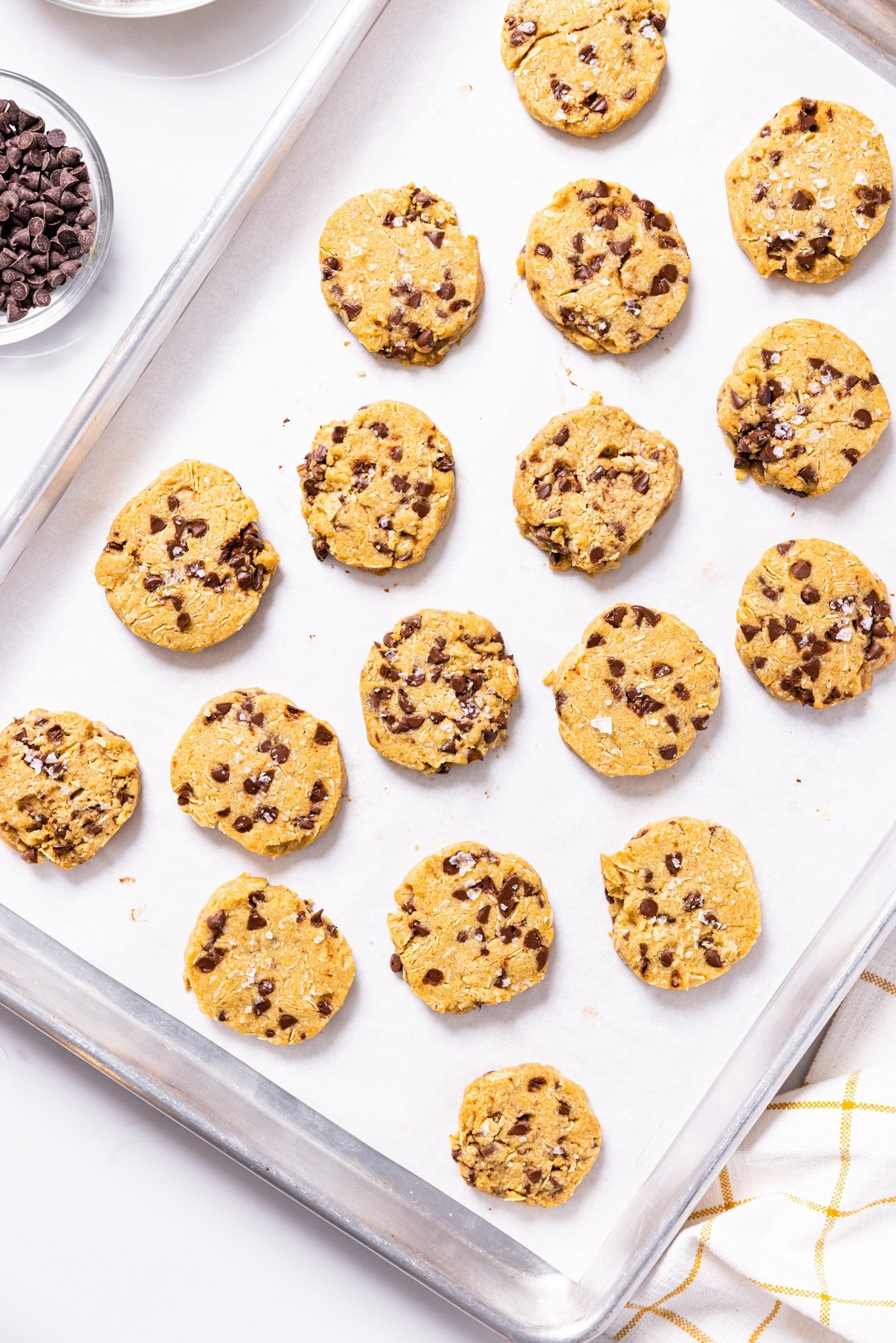 Top down view of silver baking pan filled with baked chocolate chip and oatmeal refrigerator cookies with mini chocolate chips in bowl