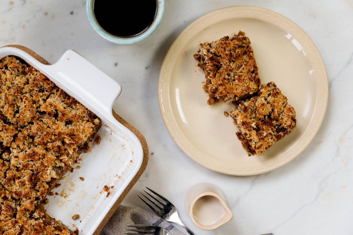 Tan plate with cup of coffee with oatmeal cake to the side in a baking dish on marble surface.