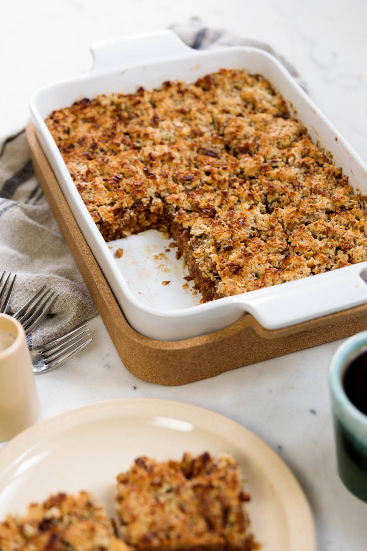 Cake with caramelized frosting on top in baking dish with forks and towel to the side on marble surface.