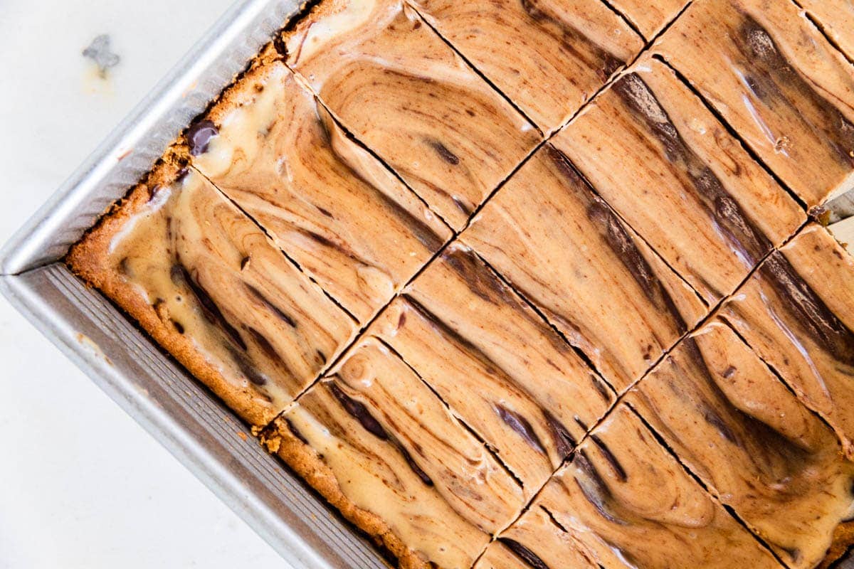 Slices of peanut butter fingers with peanut butter and chocolate swirls still in a metal baking pan after being sliced.