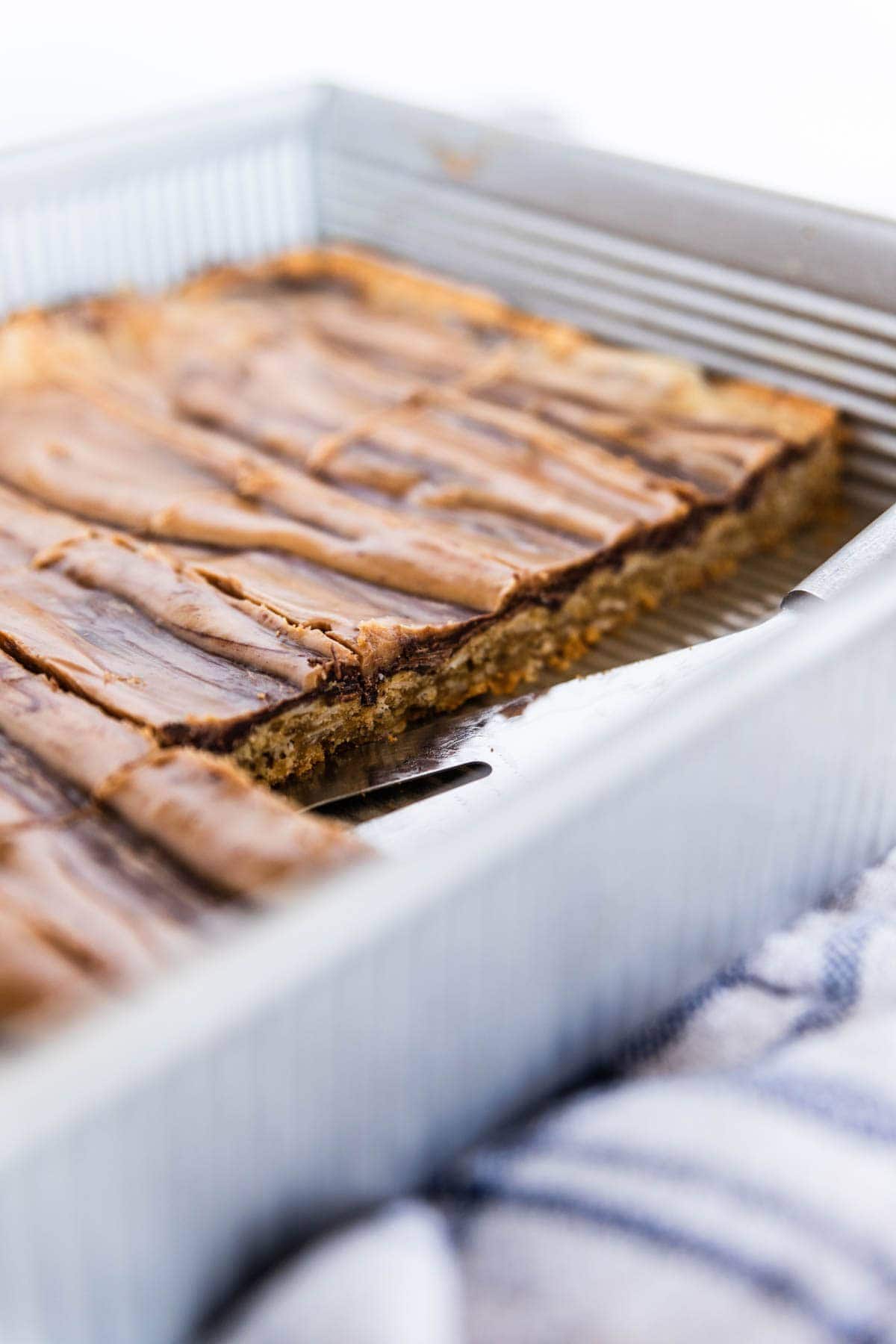 Peanut butter fingers in a metal baking dish showing the bottom layer made up of an oat texture.