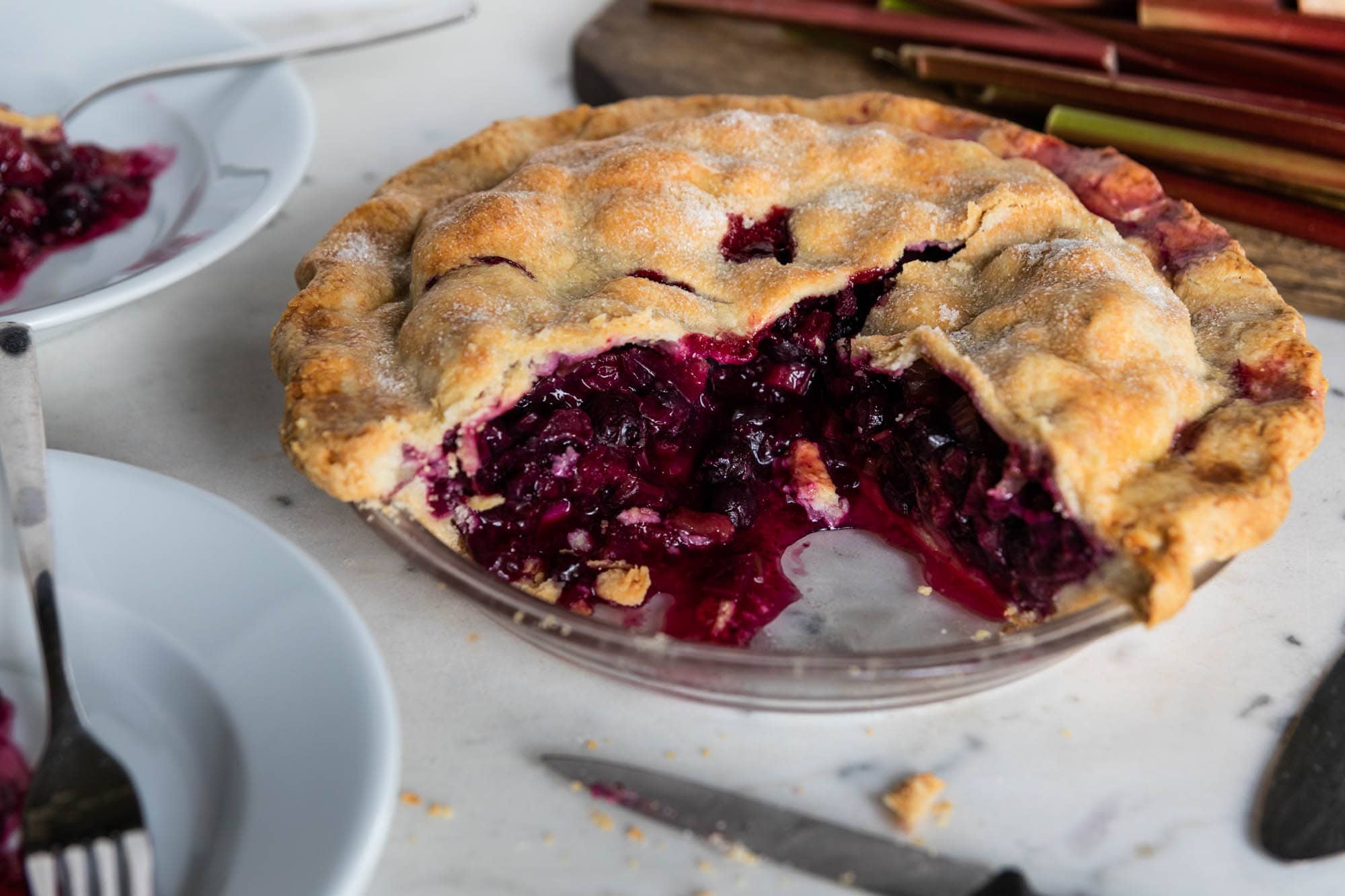 Pie with a few slices removed with filling dripping out with plates all around.