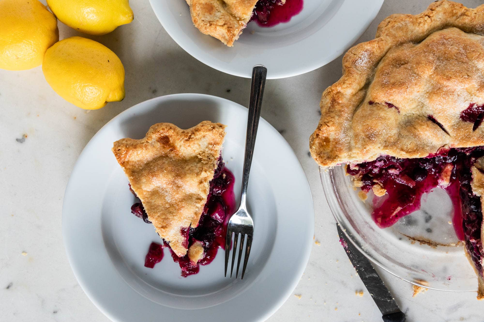 Plate with slices of pie with light brown crust with rest of pie to the side all on marble surface.