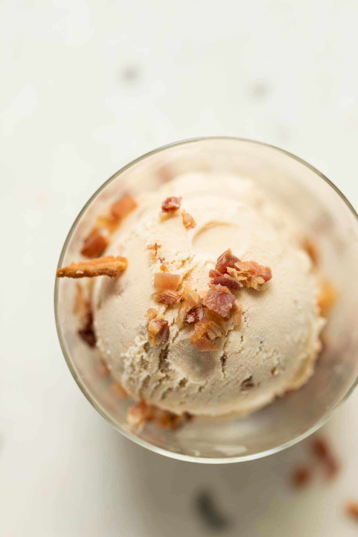 Top down view of maple bacon ice cream topped with bacon pieces in clear glass on marble surface