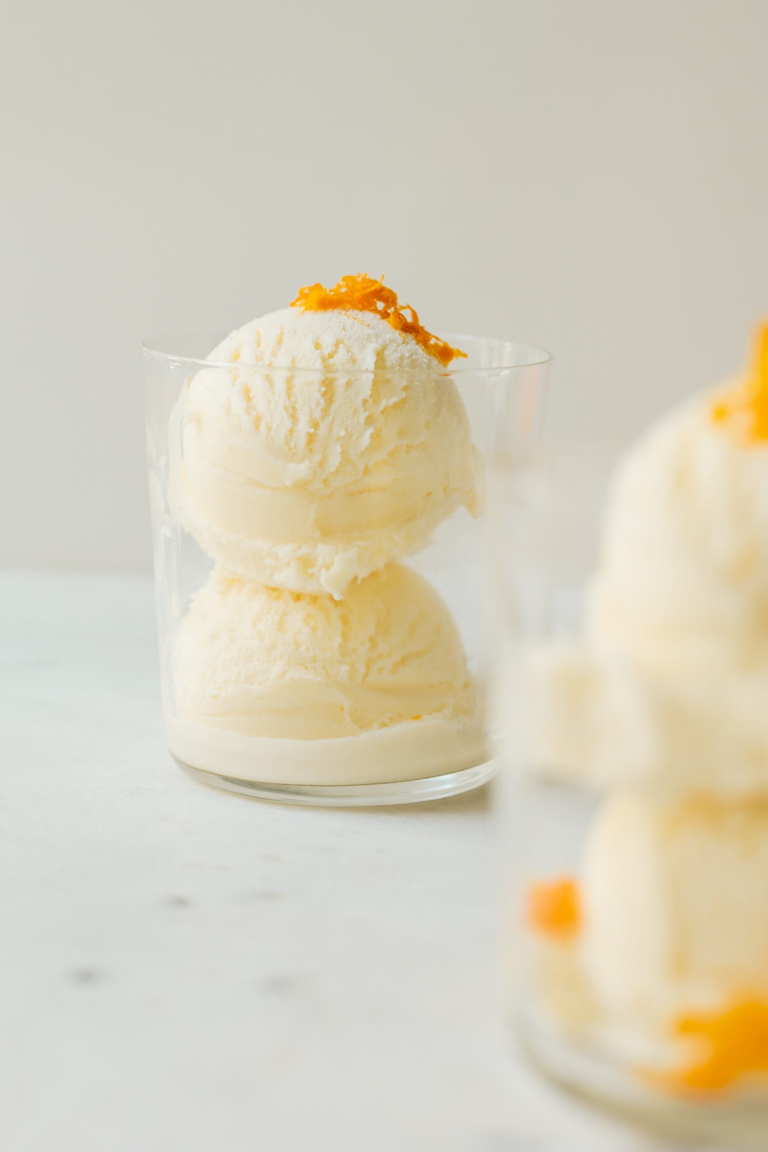 Mimosa ice cream speckled with orange zest pieces in a clear glass on marble surface with second ice cream glass in foreground