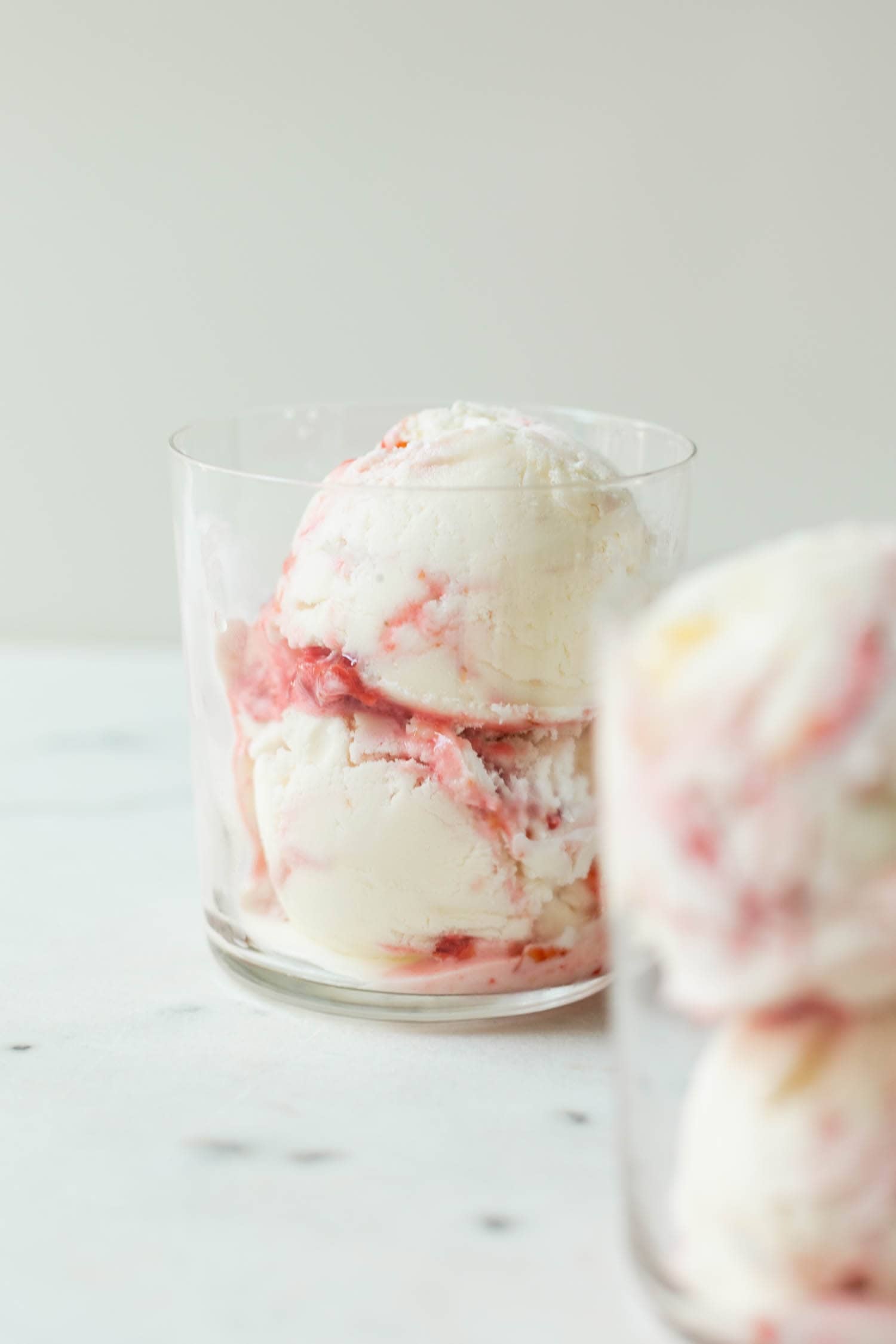 Sour cherry frozen yogurt with streaks of cherry jam throughout in clear glass with second glass in foreground on marble surface