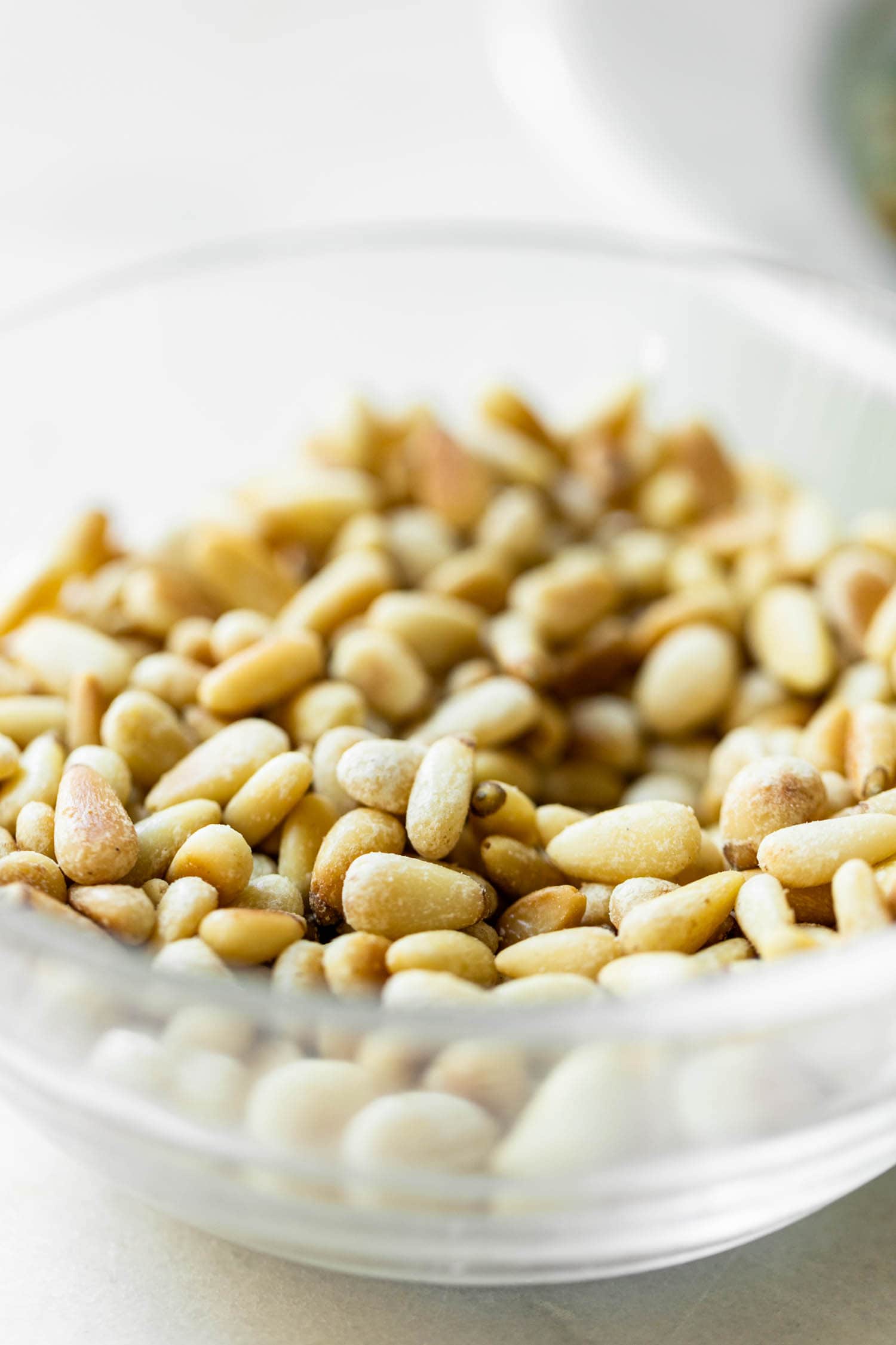 Glass bowl filled with toasted pine nuts on marble surface