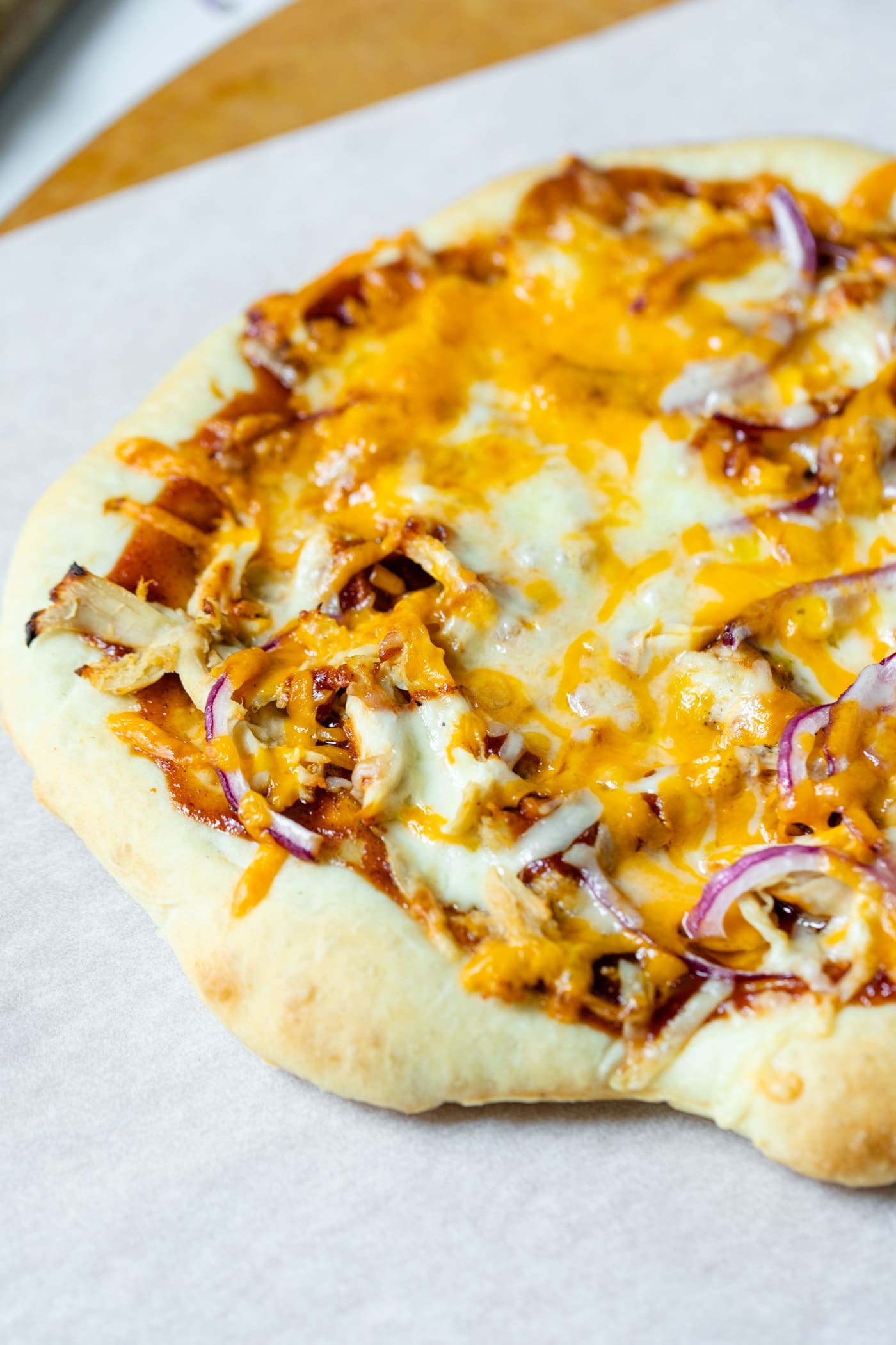 Homemade barbecue chicken pizza made of chicken, cheese, barbecue sauce and red onion on a homemade crust on a piece of white parchment and pizza board on a marble surface