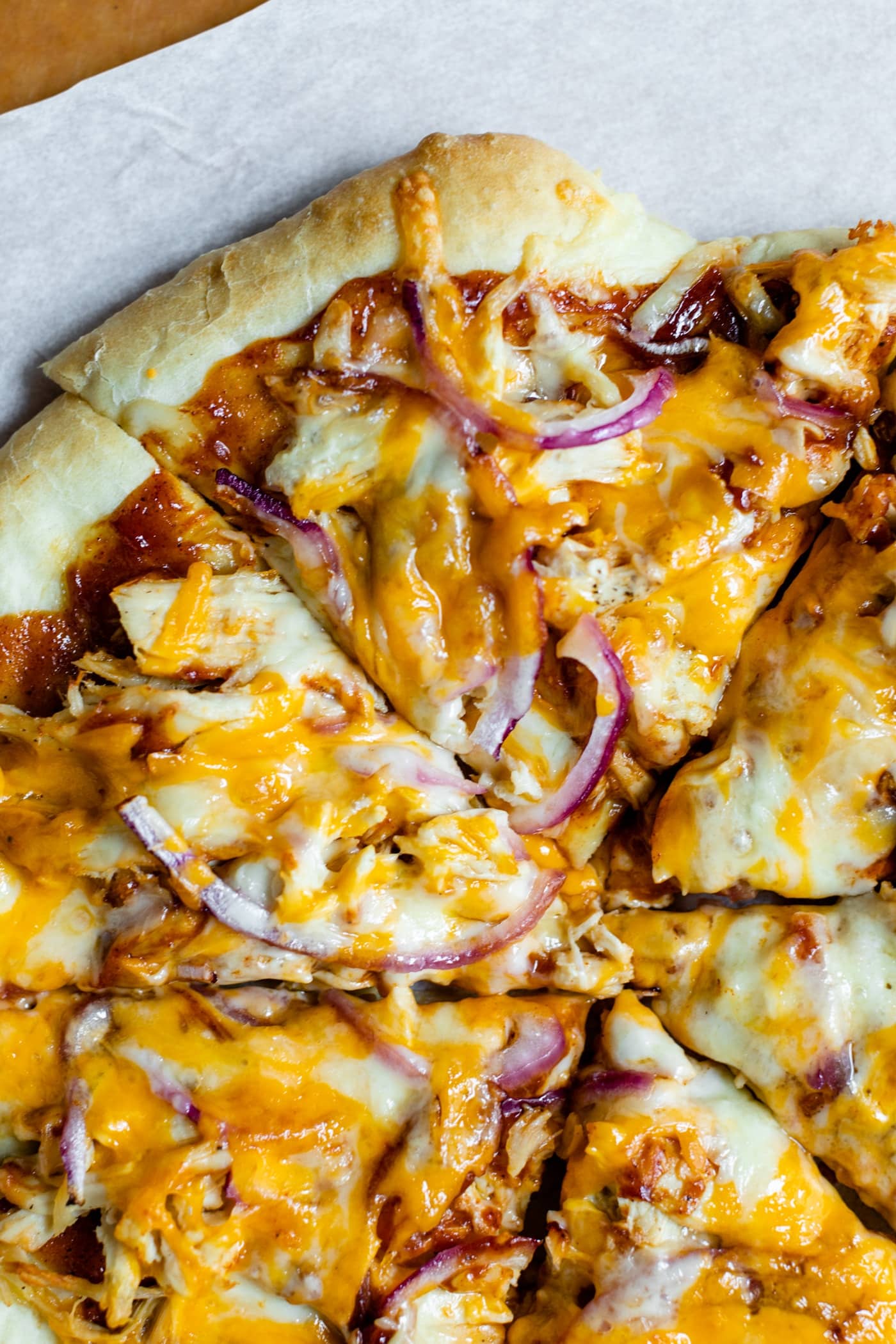 Top down view of sliced homemade barbecue chicken pizza made of chicken, cheese, barbecue sauce and red onion on a homemade crust on a piece of white parchment and pizza board