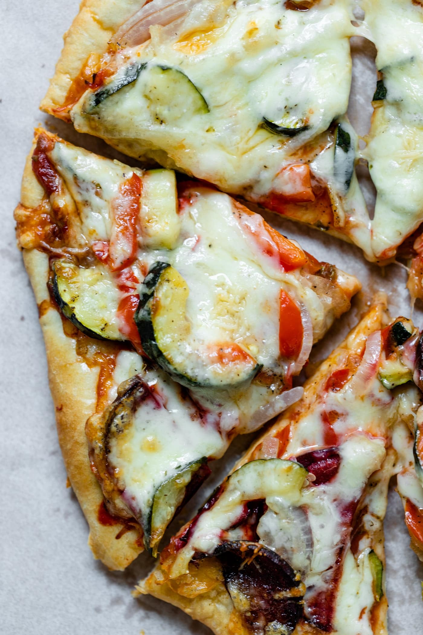 Top down view of homemade roasted vegetable pizza with vegetables and cheese on crust on top of piece of white parchment