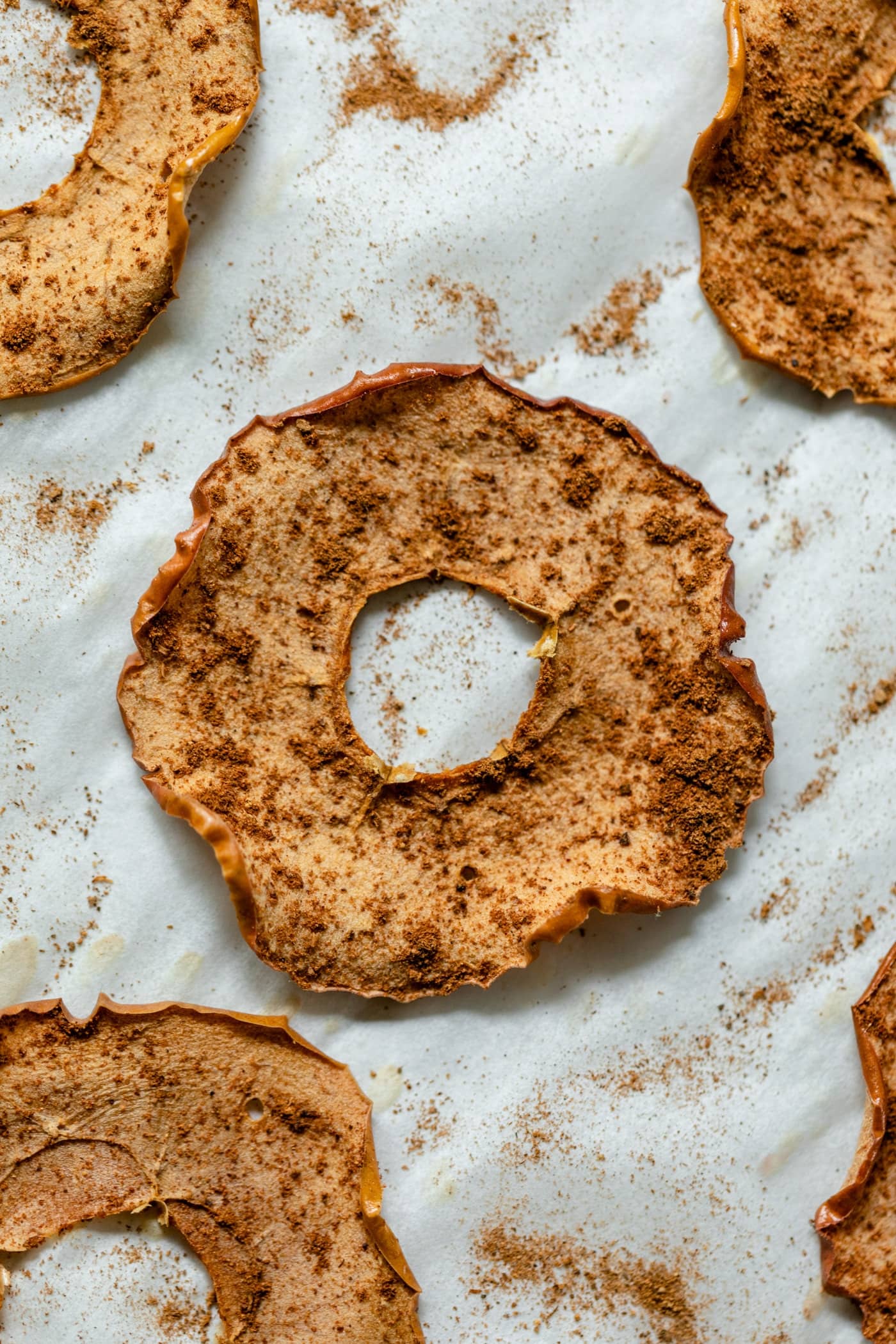 Top down view of homemade apple chips sitting on piece of white parchment and sprinkled with spices