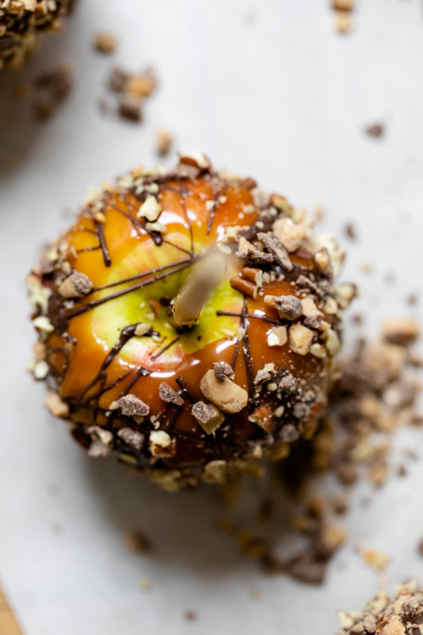 Top down view of homemade caramel apples with toffee pieces and chopped pecans sitting on white parchment