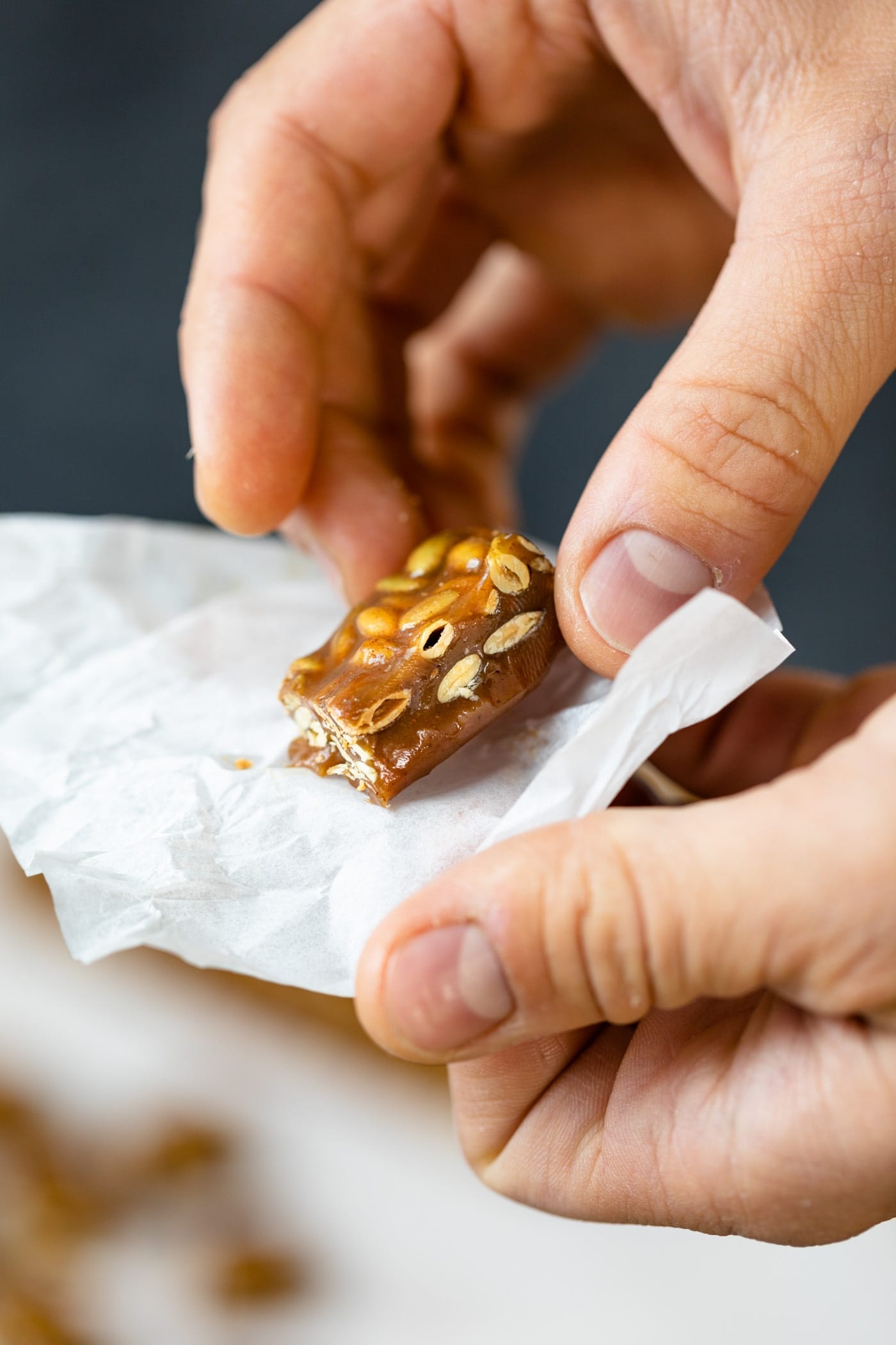 Hand holding pumpkin spice caramels in white wrapper with extra caramels in background on a gray surface