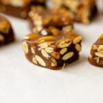 Pumpkin spice caramels sitting on piece of white parchment paper on wood board with brown bowl and extra caramel in background