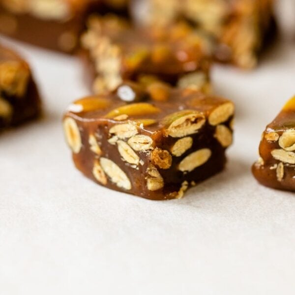 Pumpkin spice caramels sitting on piece of white parchment paper on wood board with brown bowl and extra caramel in background