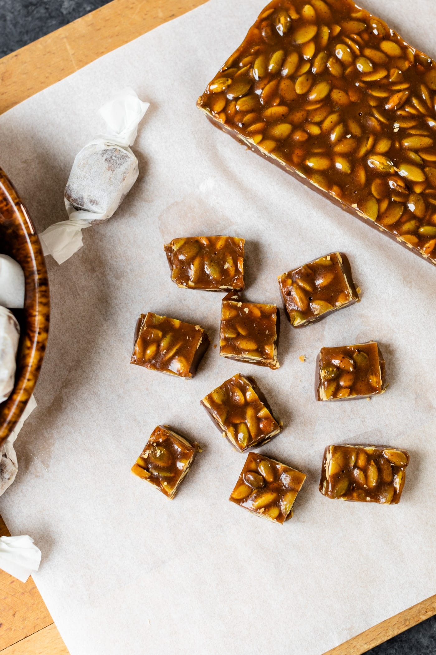 Top down view of pumpkin spice caramels sitting on white parchment on board with bowl containing wrapped caramels all on gray slate surface