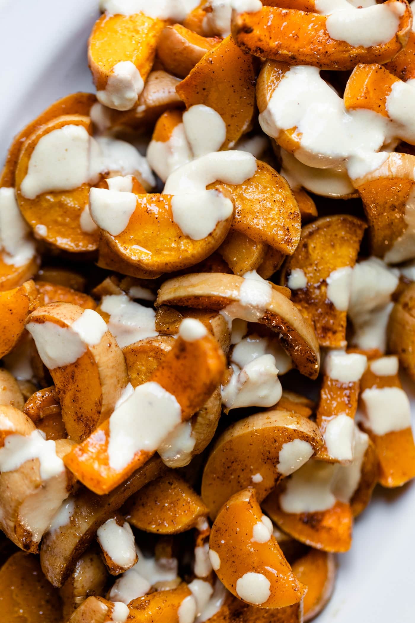 Spiced butternut squash drizzled with white tahini sauce sitting on white platter