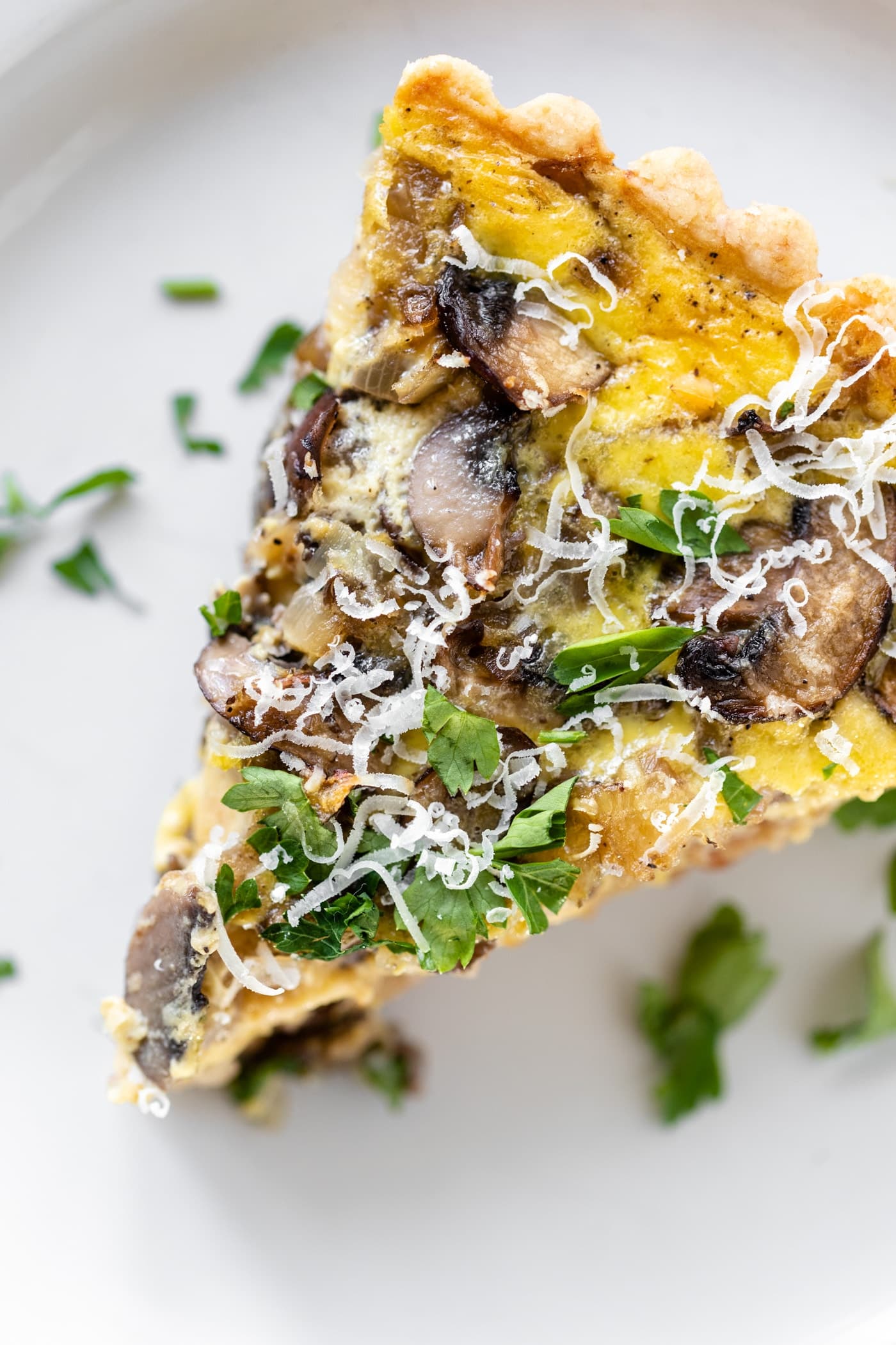 Piece of breakfast quiche topped with parsley and Parmesan cheese sitting on white plate