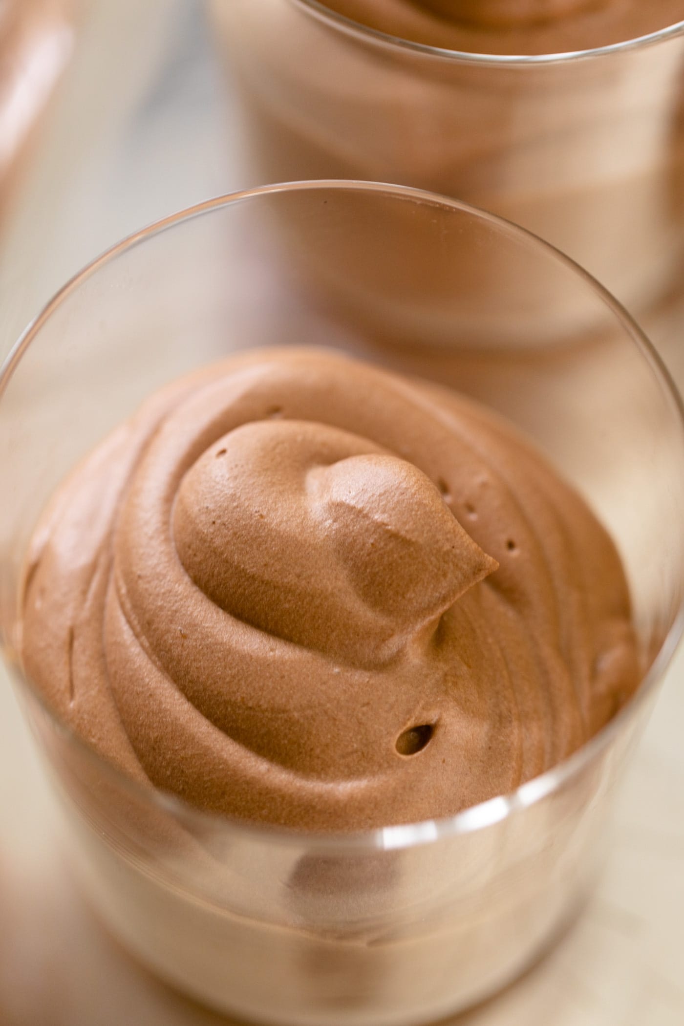 Chocolate mousse sitting in glass container on silver tray with extra glasses of mousse in background.