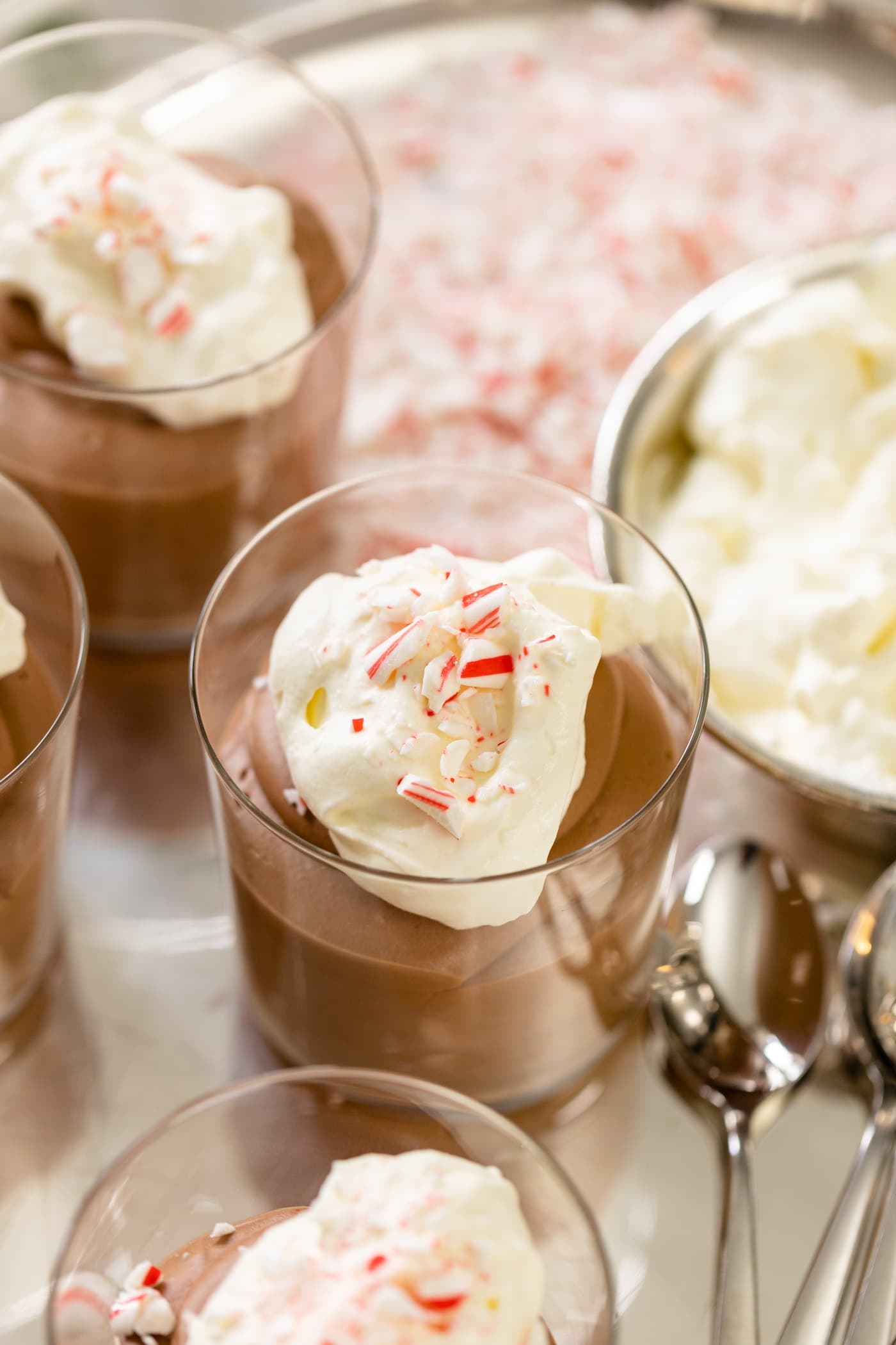 Chocolate mousse in glass topped with whipped cream and peppermint bits with extra glasses and peppermint bits in background all on silver tray.