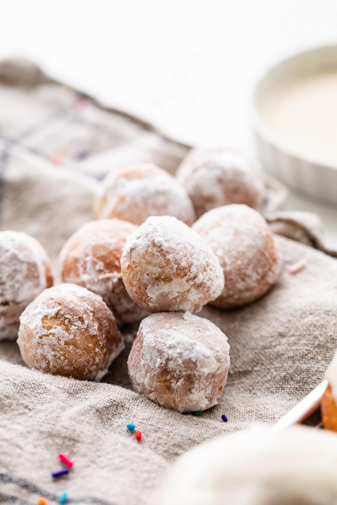 Pile of homemade donut holes topped with powdered sugar sitting on linen towel