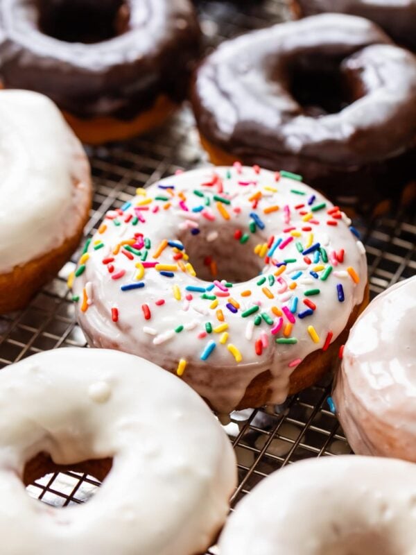 Homemade yeast donuts topped with vanilla and chocolate glazes and sprinkles sitting on wire rack