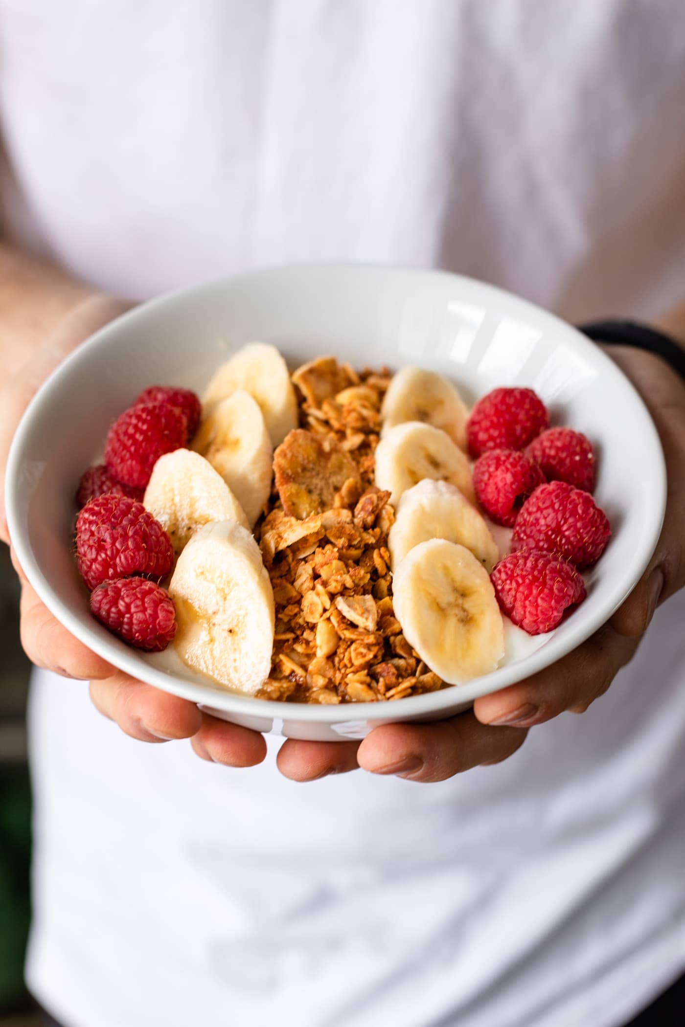 Hands holding bowl of peanut butter granola with white shirt and black pants in background