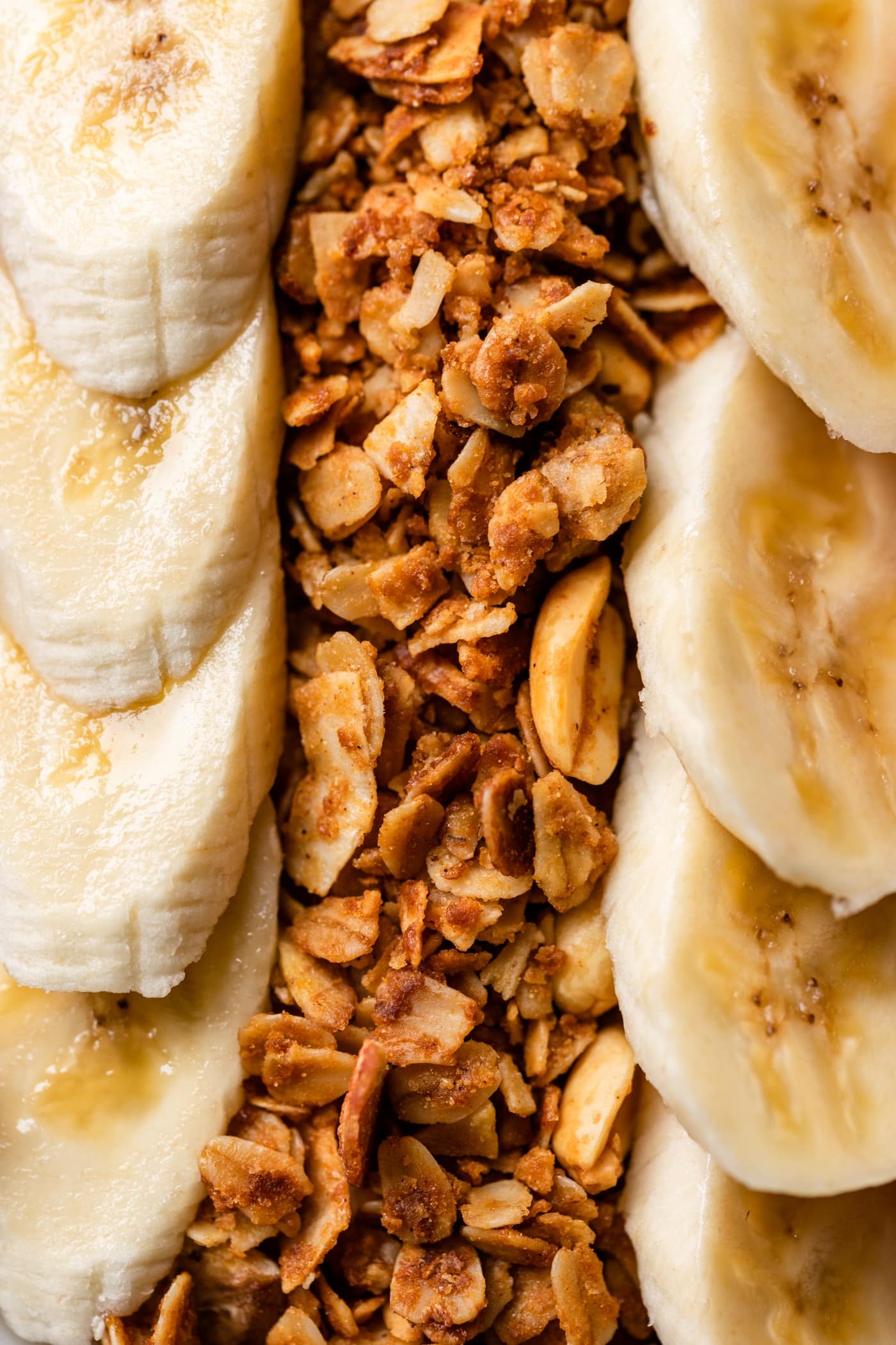 Close up view of homemade peanut butter granola nestled in between slices of banana