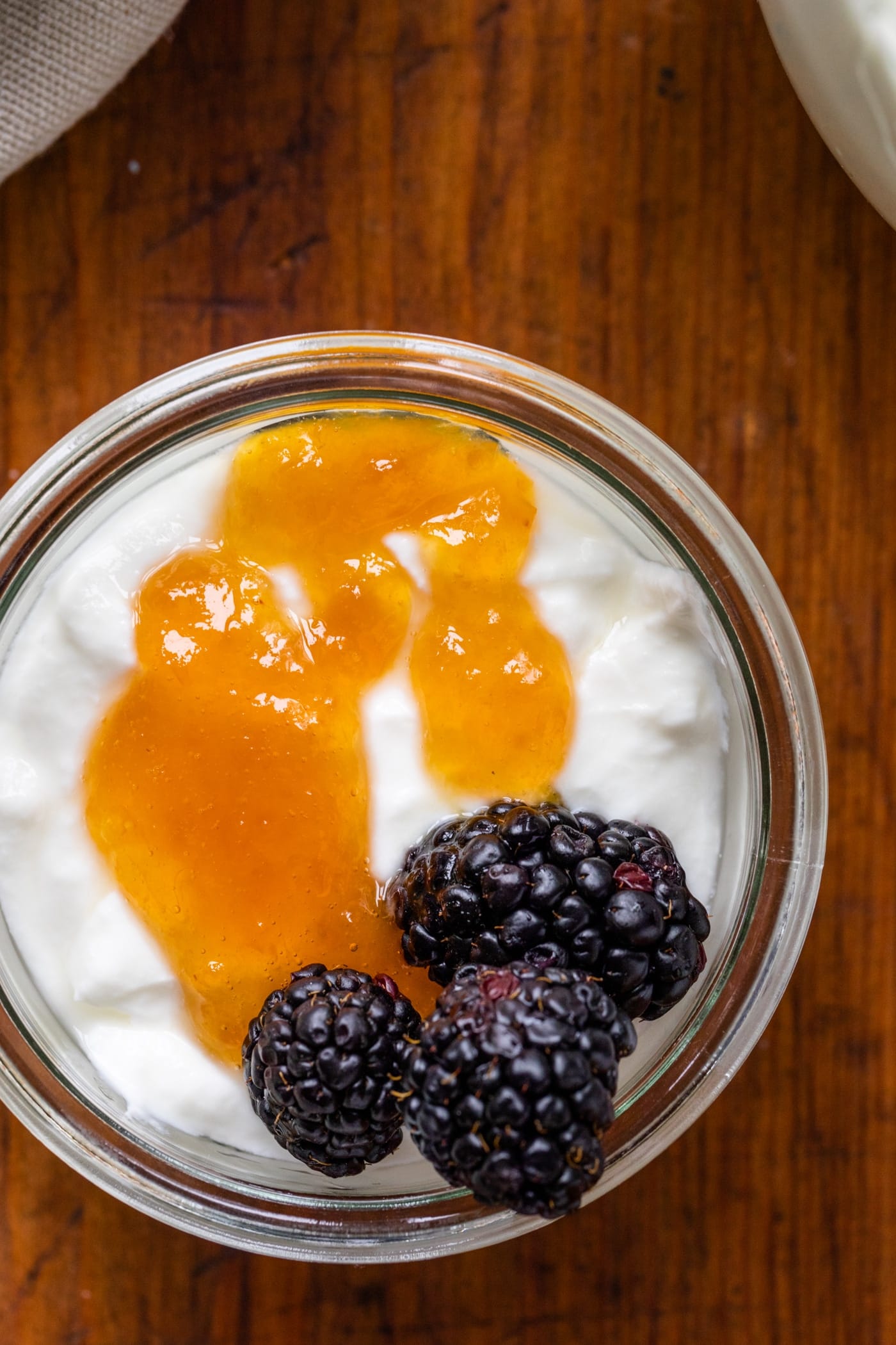 Top down view of homemade yogurt topped with peach preserves and blackberries in glass container sitting on wood board