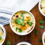 Top down view of egg, ham, and sweet potato casserole in small white ramekin dishes with towel all on wood surface
