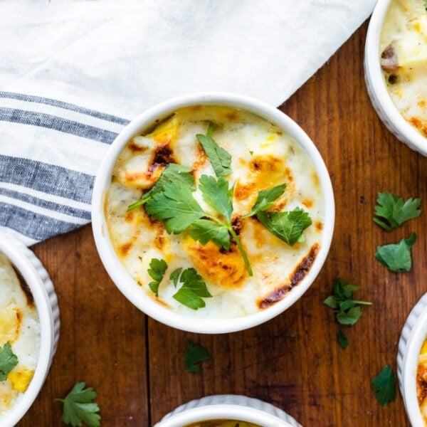 Top down view of egg, ham, and sweet potato casserole in small white ramekin dishes with towel all on wood surface