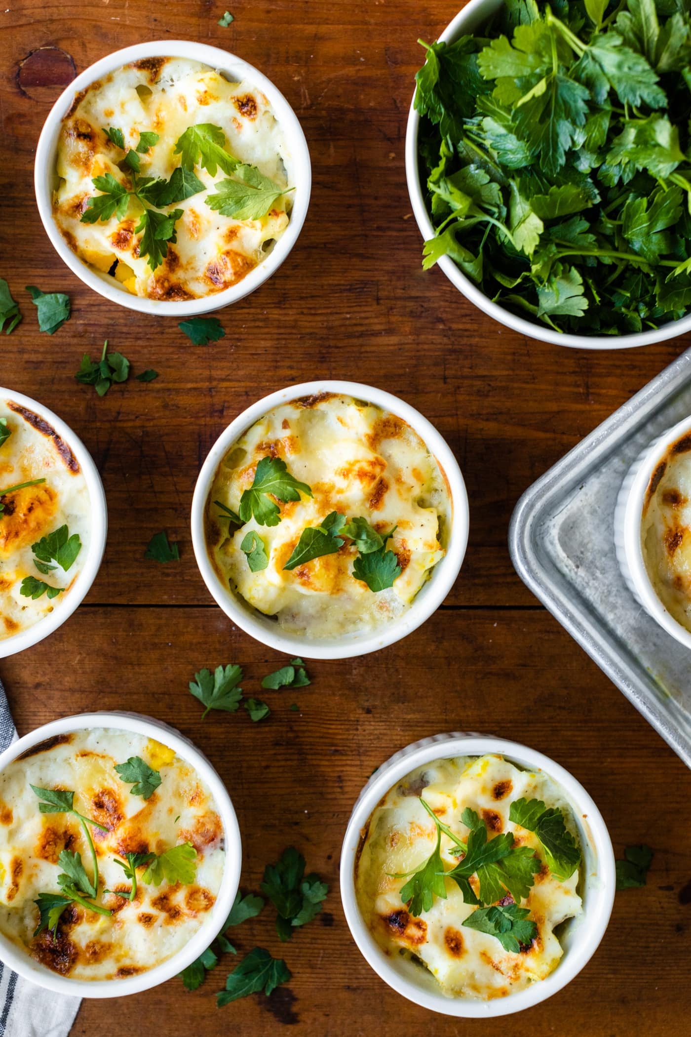 Top down view of egg and sweet potato casserole sitting in white ramekin dishes with bowl of parsley to the side all on wood surface