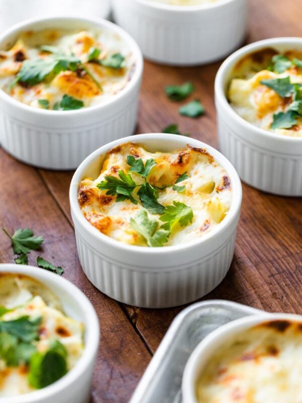 White ramekins sitting on wood board with towel in background filled with egg casserole and topped with parsley