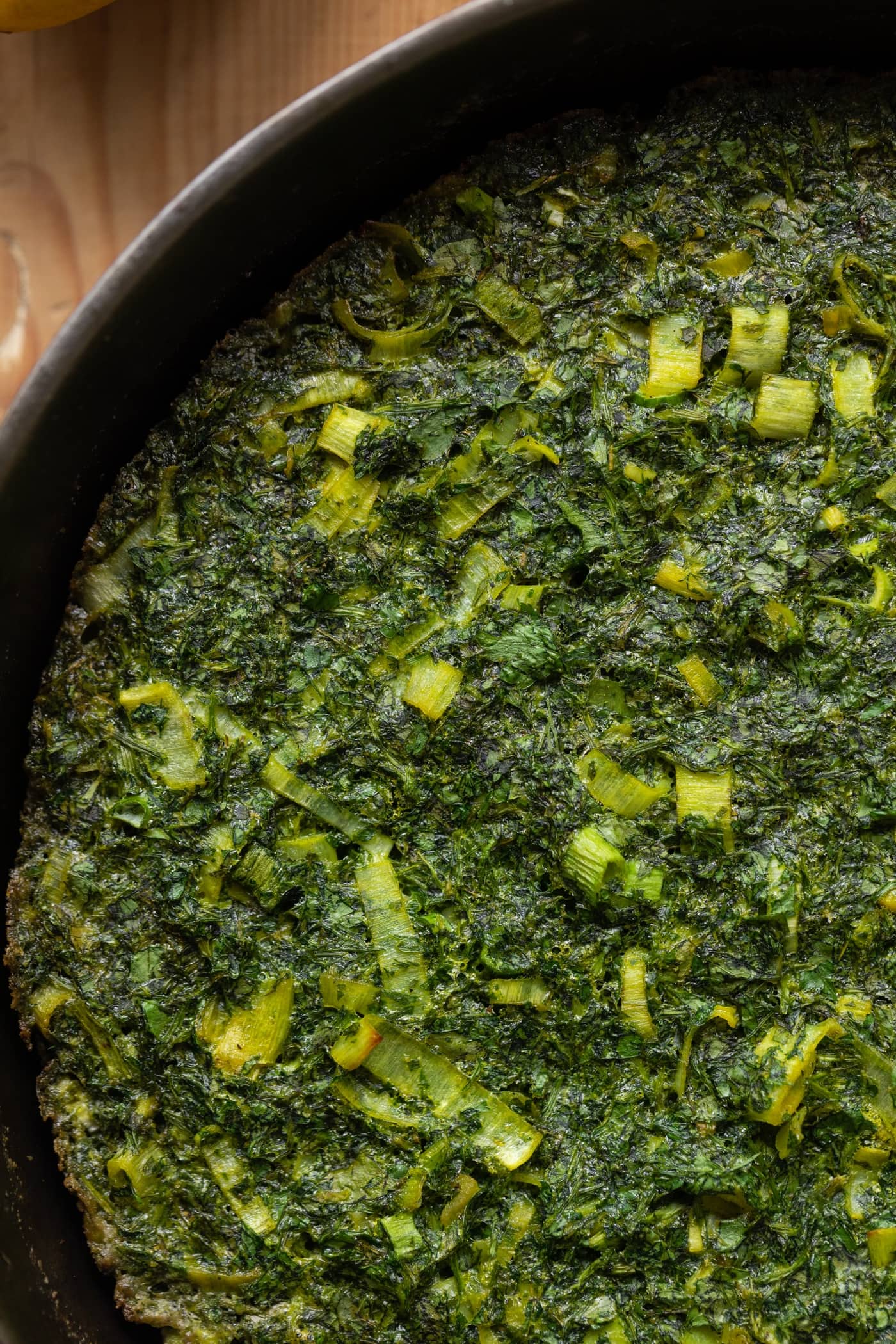 Top down view of herb omelet dotted with leeks and herbs in cast iron skillet on wood surface