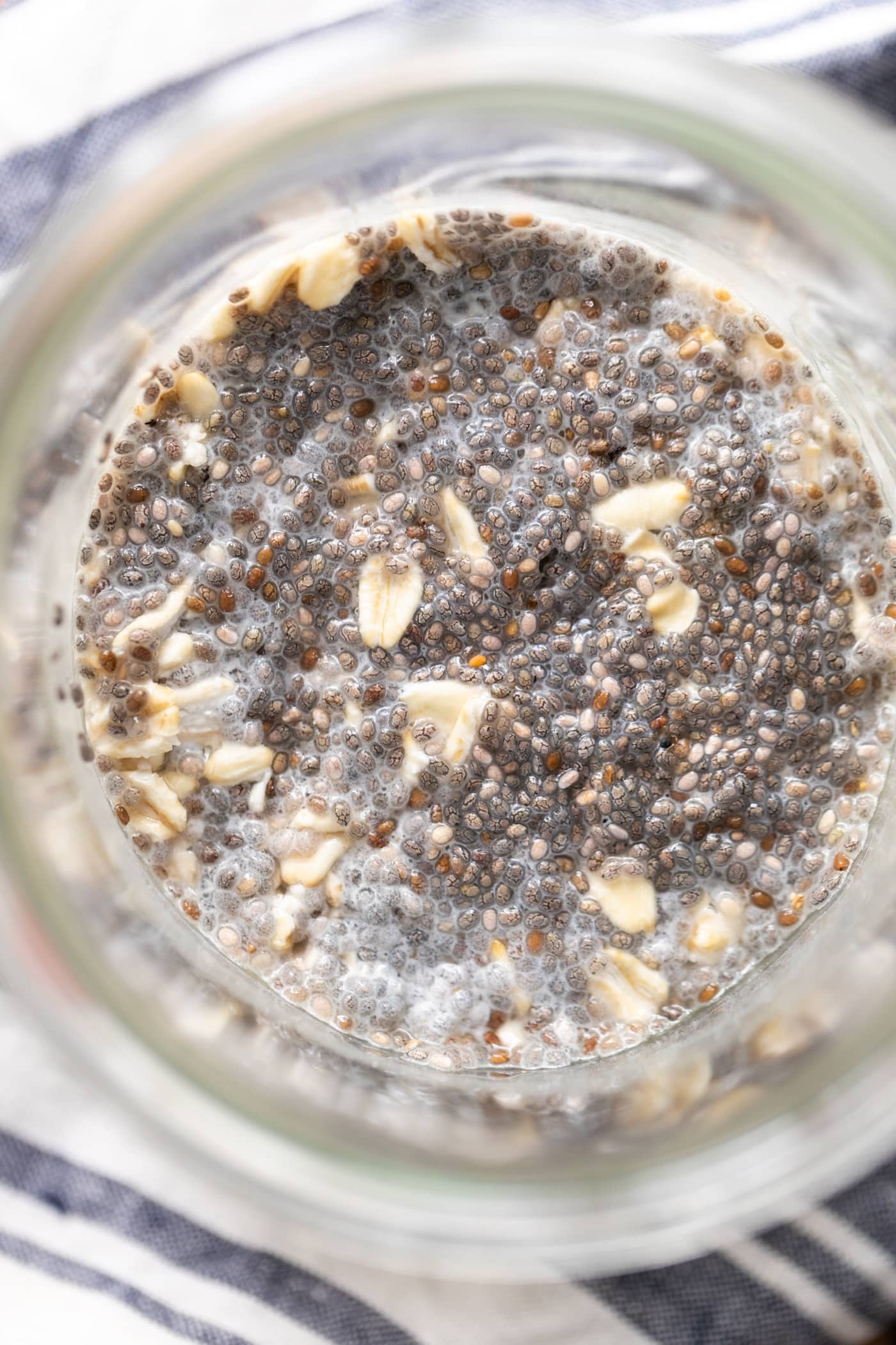 Top down view of chia seeds sitting in oatmeal in glass container with striped linen underneath