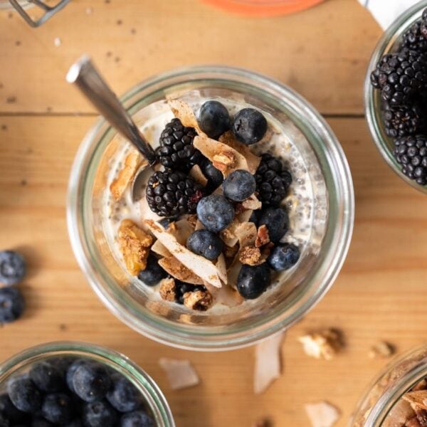 Top down view of vegan overnight oats in glass container with blueberries and granola on top all on wood surface