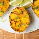 Top down view of three mangoes with grill marks and sprinkled with spices and cilantro sitting on white plate on a wood table with limes