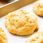 Peach drop biscuit sitting on piece of white parchment on baking sheet with wood surface in background