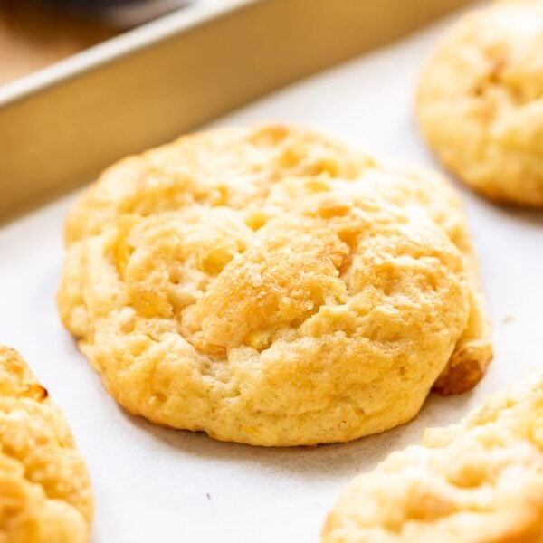 Peach drop biscuit sitting on piece of white parchment on baking sheet with wood surface in background
