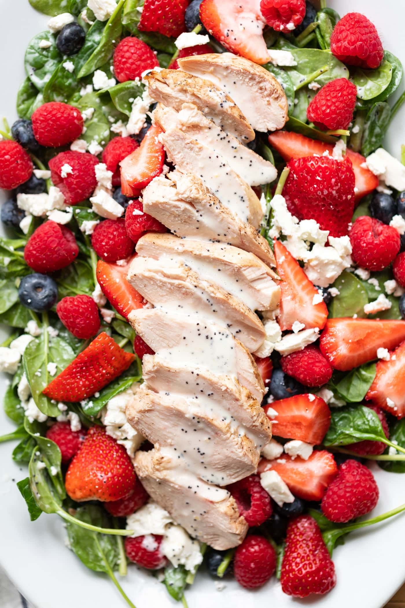Pieces of grilled chicken layered on top of spinach with berries and drizzled with poppy seed dressing sitting on white plate.