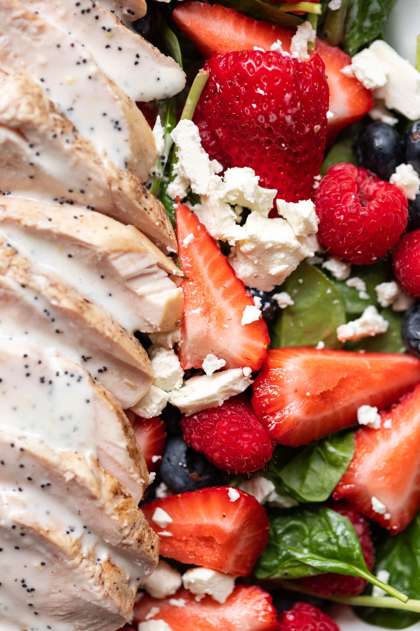 Pieces of strawberry and whole raspberries sitting on bed of spinach sprinkled with feta and layered with grilled chicken topped with lemon poppy seed dressing.