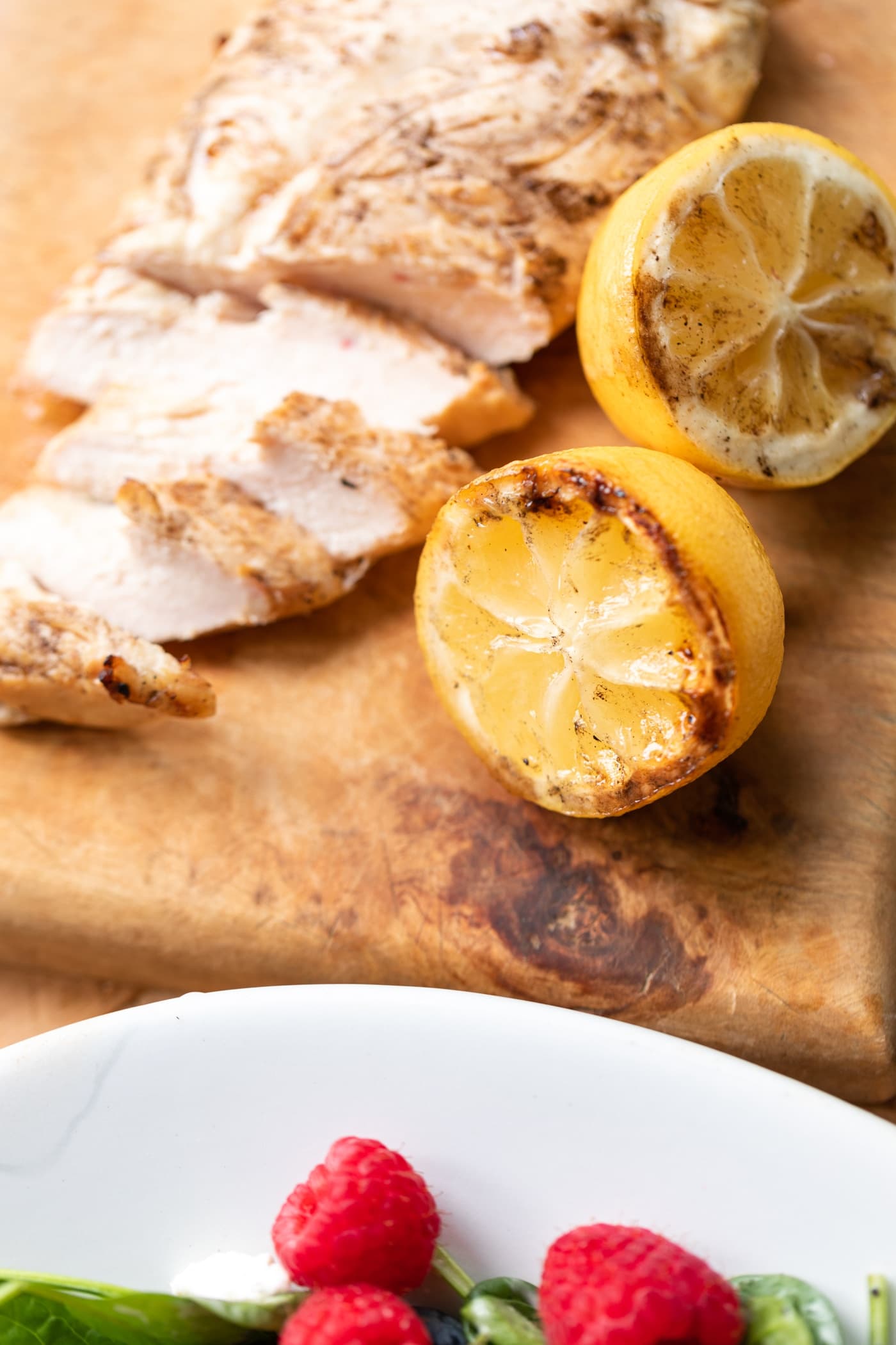 Used lemons sitting on wood cutting board with sliced chicken.