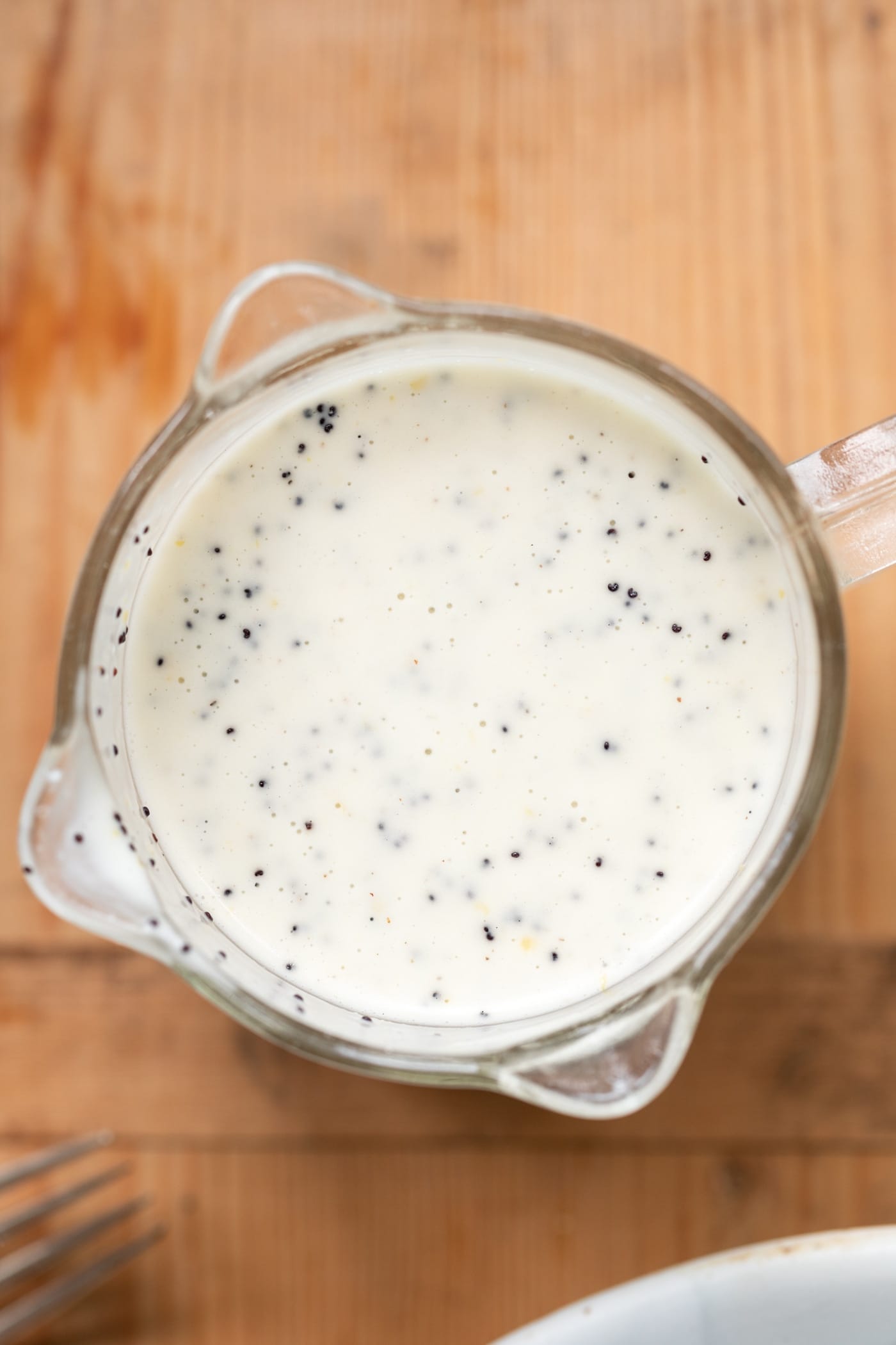 Top down view of lemon poppy seed dressing sitting in glass measuring cup on wood surface.