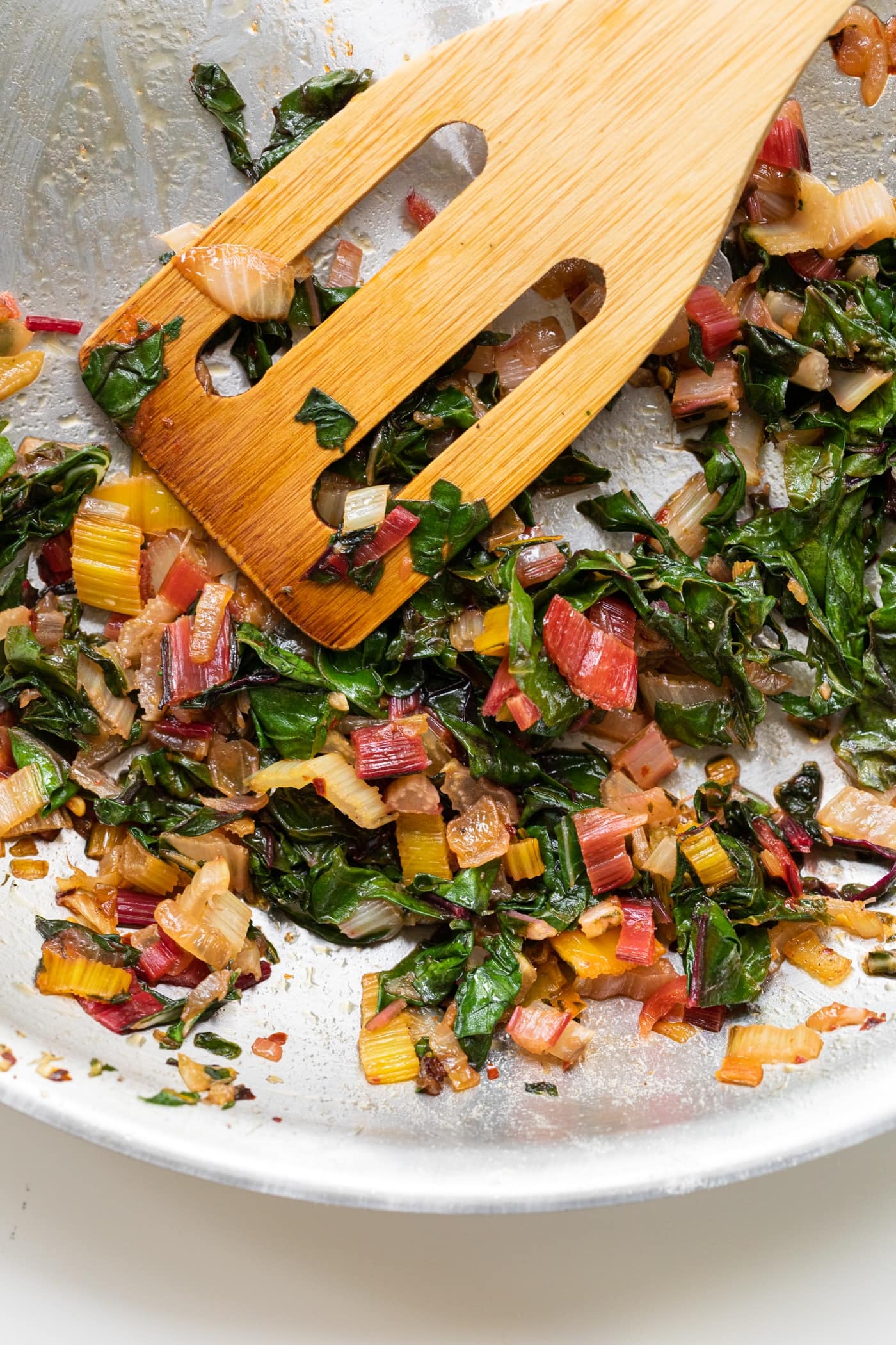 Wooden spatula sitting amongst Swiss chard mixture after being cooked on stove in stainless steel pan