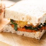 Swiss chard and harissa egg sandwich layered with homemade aioli sitting on wood cutting board with white background