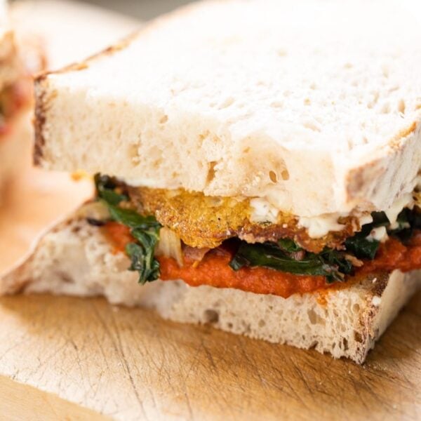 Swiss chard and harissa egg sandwich layered with homemade aioli sitting on wood cutting board with white background